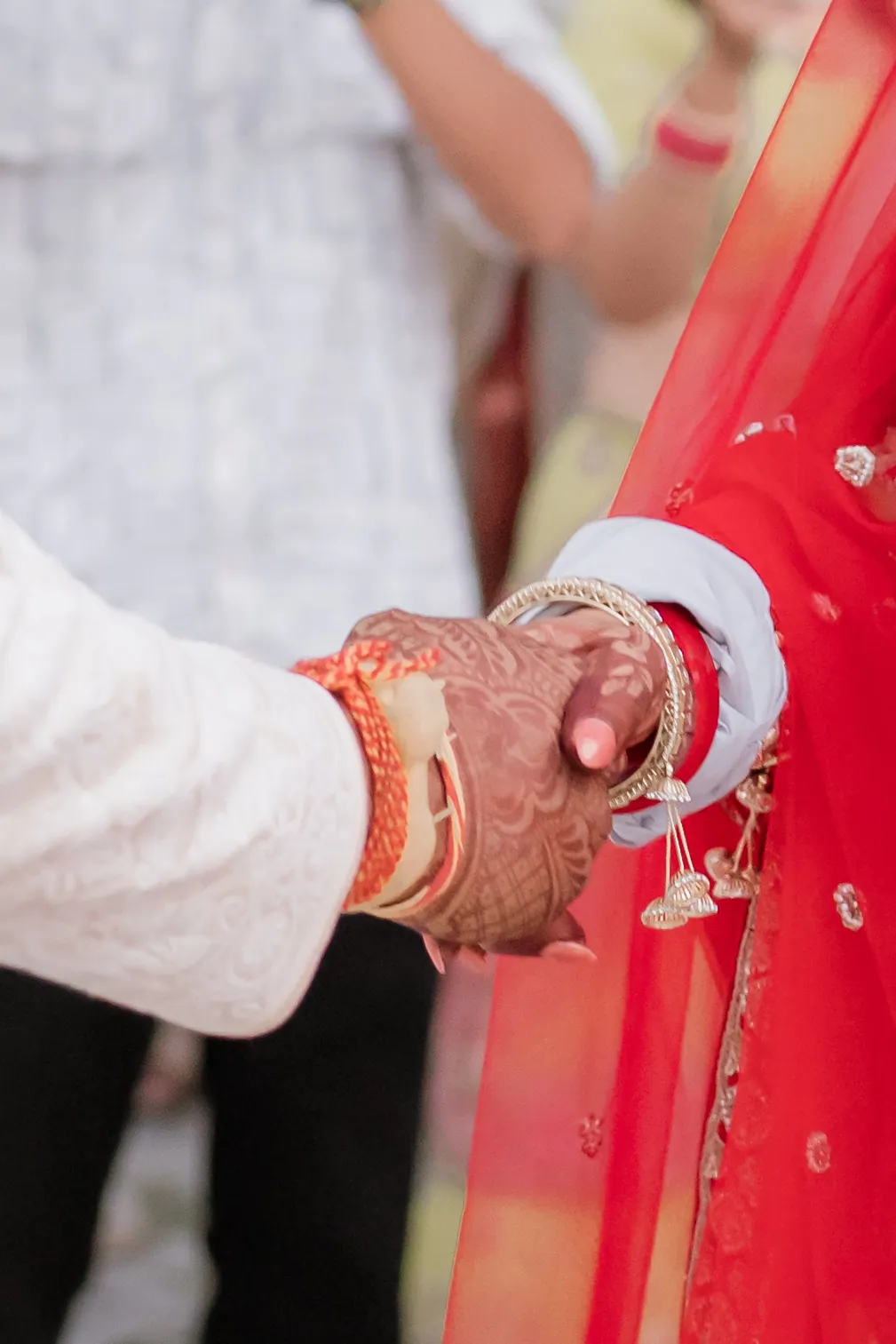 The groom's hand holding the bride's hennaed hand, red bangles on her wrist